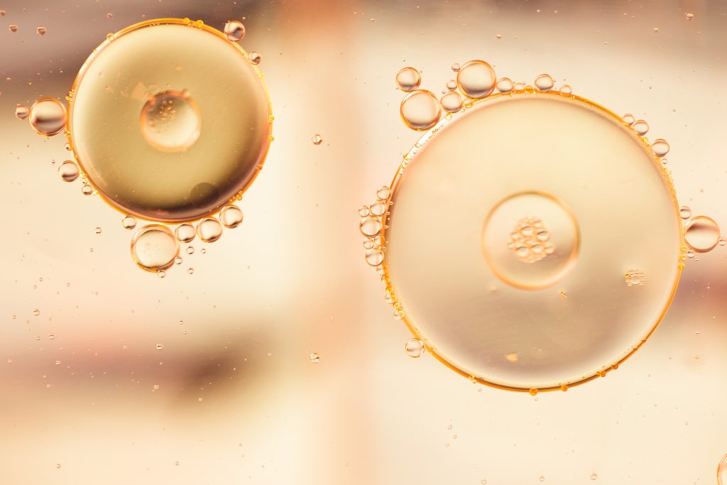Abstract close-up of water and oil mixing, forming colorful liquid droplets with bubbles, symbolizing skincare formulations and cosmetic ingredients.