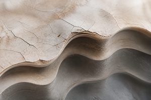 Close view of layered stone-like surface with fine cracks, smooth contours, and soft shadows in neutral beige and slate tones.